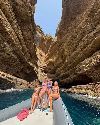Groupe d'amies à bord d'un semi-rigide de L'Eden Boat pour un EVJF dans les Calanques, falaises calcaires en arrière-plan sous le soleil provençal