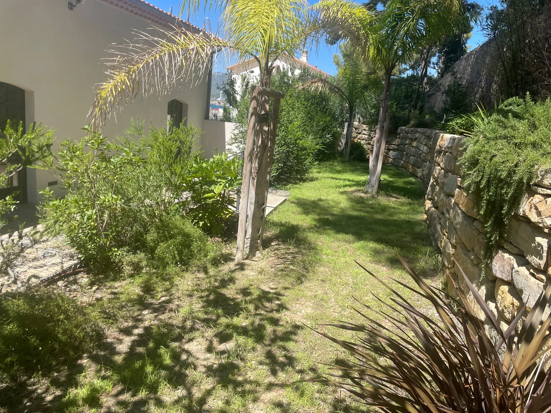 Entretien paysager d'un jardin privé à La Seyne-sur-Mer : tonte du gazon, taille des végétaux et mise en valeur des palmiers, massifs et murets en pierre par Jardivar.