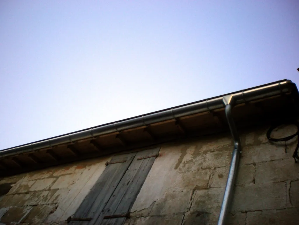 Installation de gouttières en zinc pour l'évacuation efficace des eaux pluviales sur une toiture traditionnelle de maison