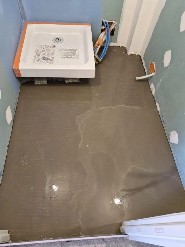 Après la réparation de la colonne de chute collective fuyarde en PVC de Ø 100 mm, réalisation d'un enduit de lissage (ragréage) et pose d'un receveur de douche surélevé sur pieds réglables pour corriger la pente d'évacuation.