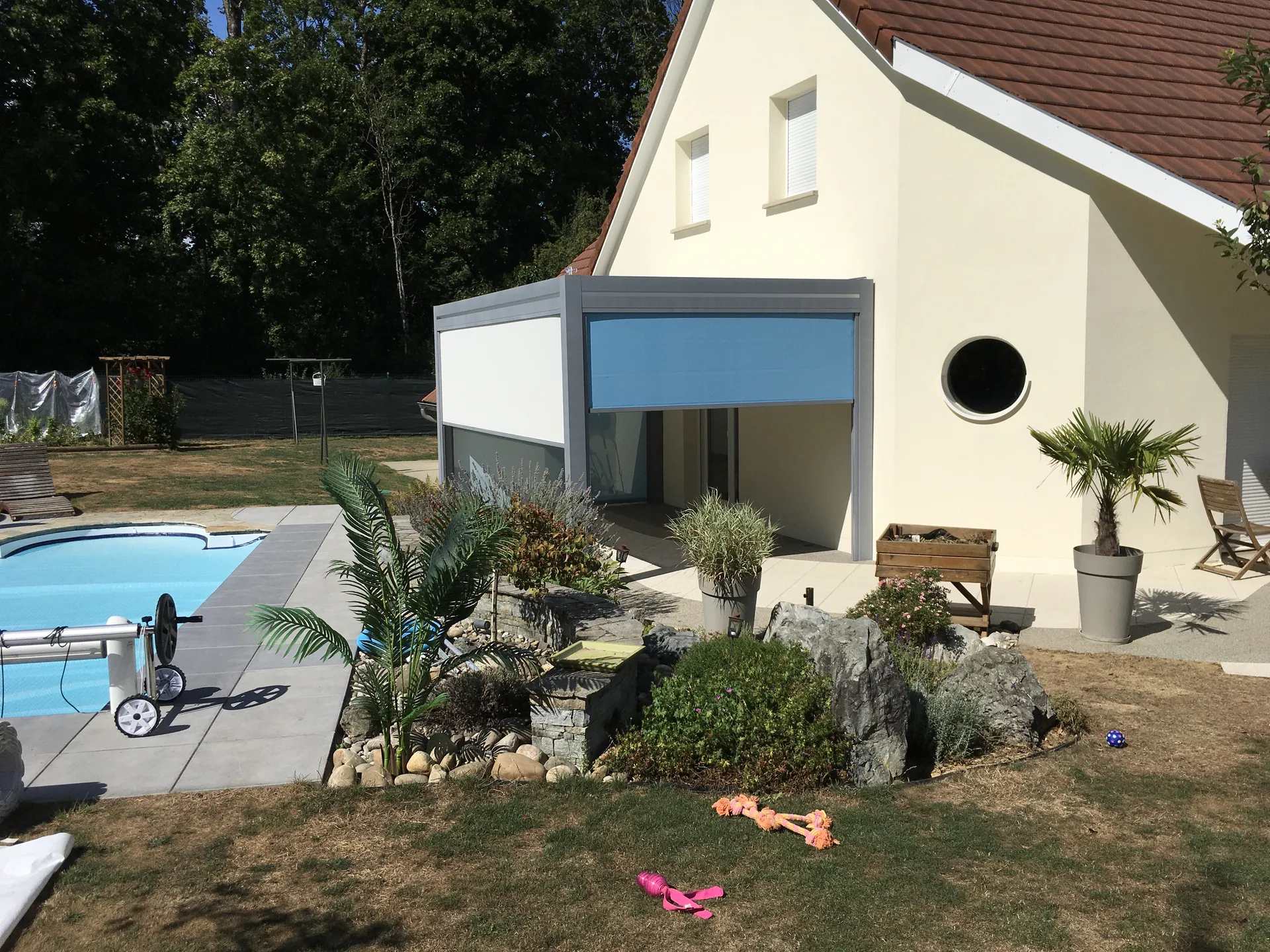 RÉALISATION AU BORD D'UNE PISCINE D'UNE PERGOLA BIOCLIMATIQUE EN ALUMINIUM GRIS CLAIR ATTENANTE AVEC STORES ET LED INTÉGRÉ