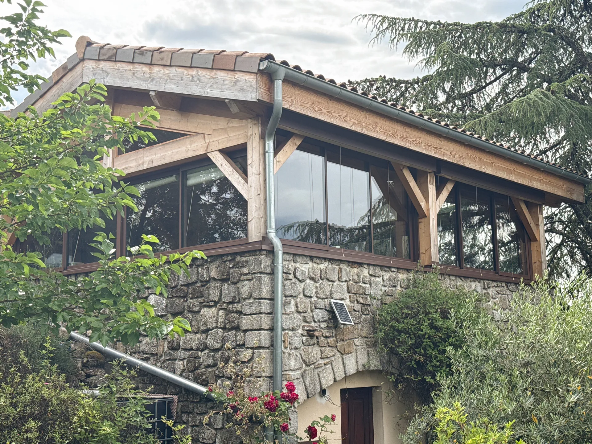 Fermeture d'une terrasse ardéchoise sous charpente bois avec de grands coulissants aluminium teinte rouille
