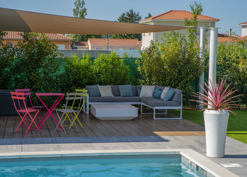 Aménagement paysager avec terrasse bois, gazon synthétique et voiles d’ombrage autour d’une piscine à Genas (69740)