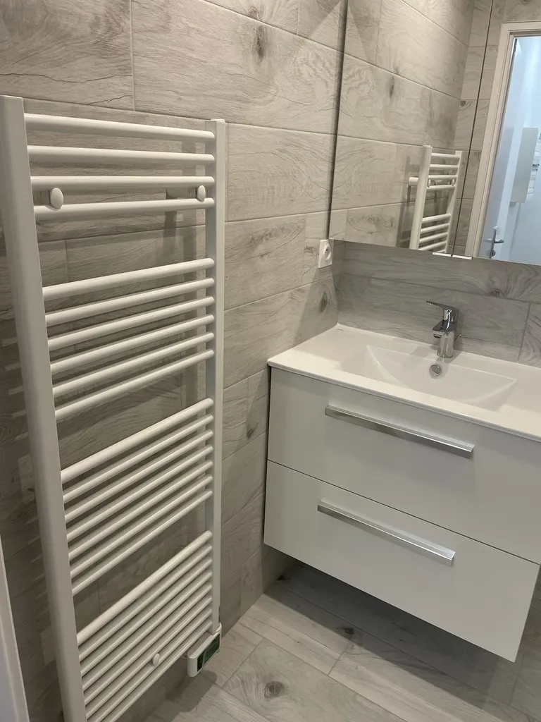 Pose des équipements sanitaires finaux : meuble vasque suspendu Alterna Concerto, armoire de toilette miroir Bruges et radiateur sèche-serviettes électrique à fluide caloporteur Primeo2 de 750 W.
