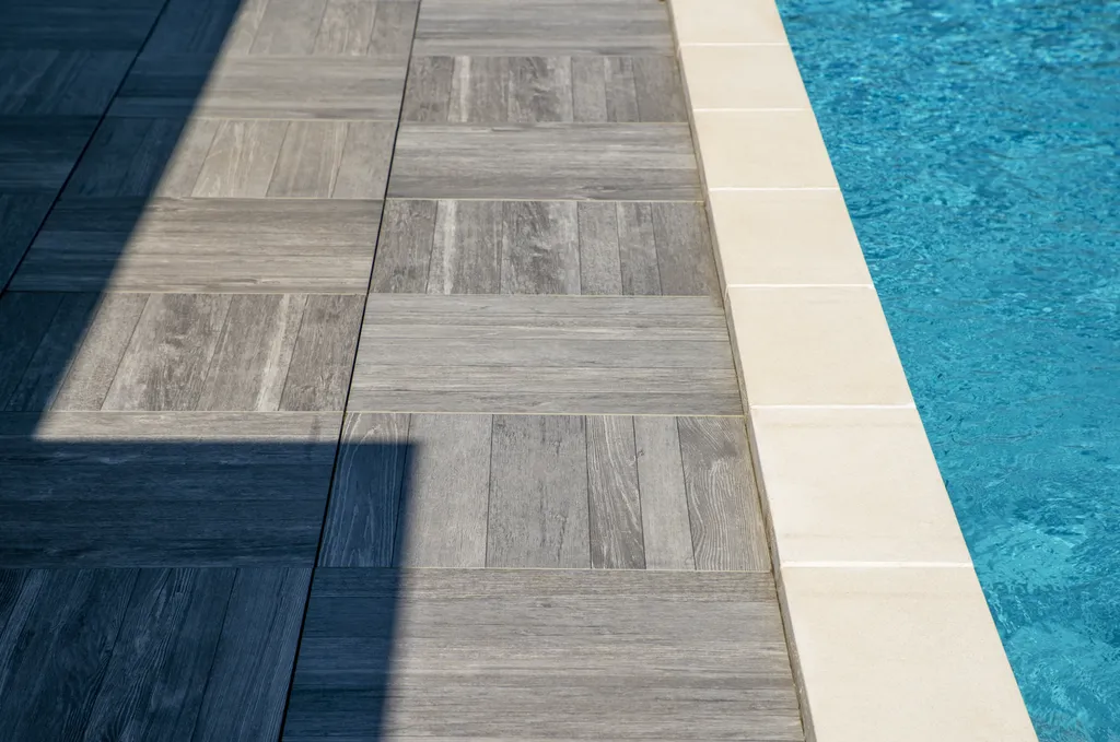 Aménagement paysager avec terrasse bois, gazon synthétique et voiles d’ombrage autour d’une piscine à Genas (69740)